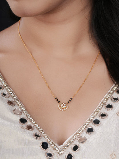Gold necklace with a small pendant on a person wearing a white blouse with black accents.